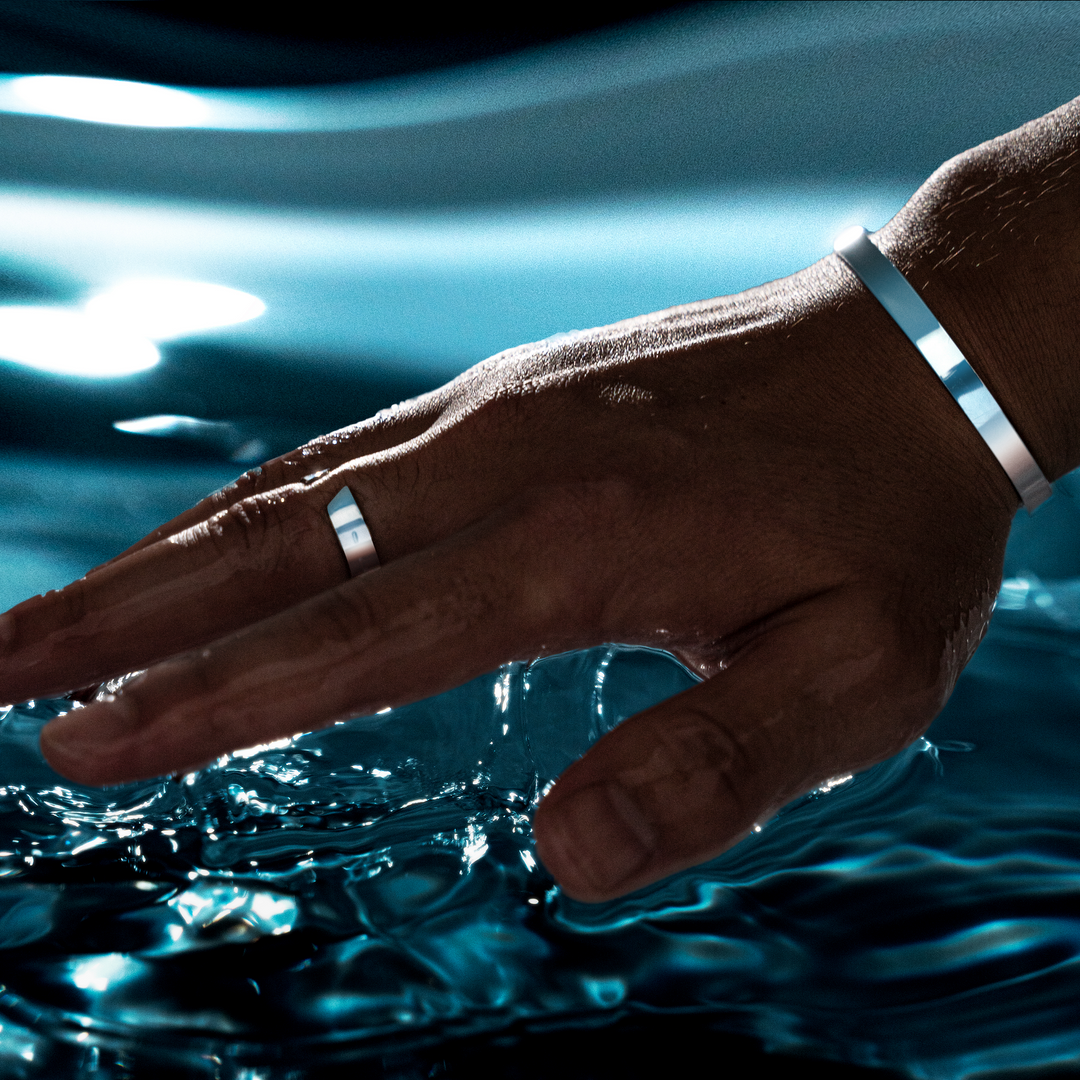 Hand mit silbernem Ring und Armband über Wasseroberfläche, Schmuck für Männer.