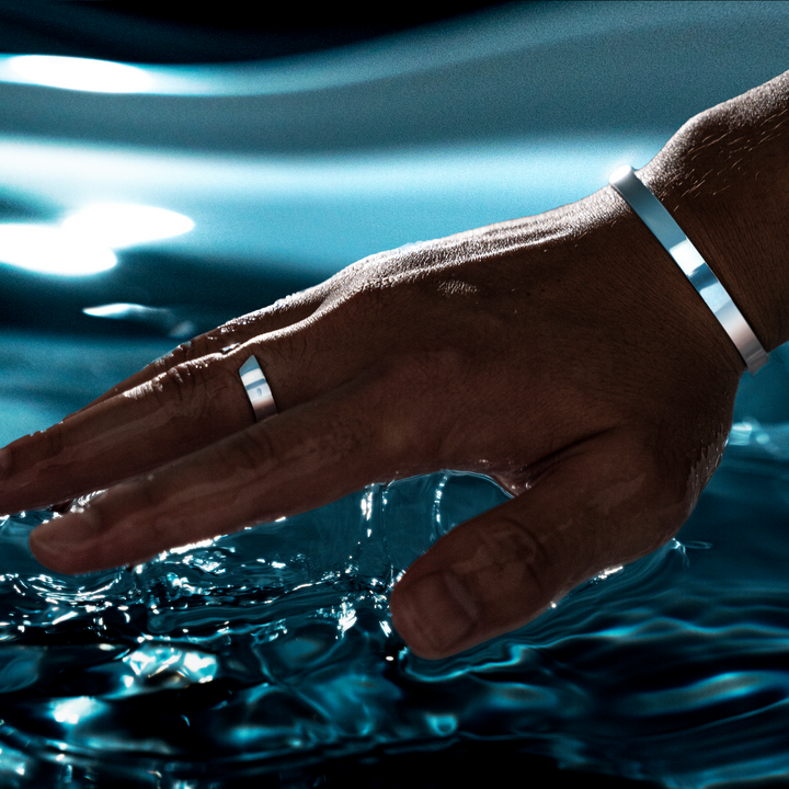 Hand mit silbernem Ring und Armband über Wasseroberfläche, Schmuck für Männer.