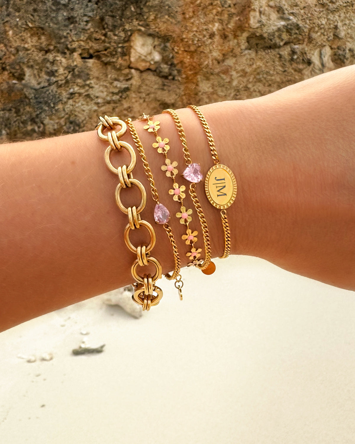 Goldene und rosa Armbänder-Set, Damenmode, Schmuck, Blumenmuster, Strandhintergrund.
