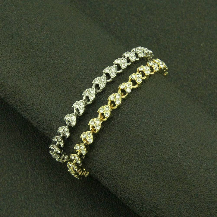 Zwei Armbänder, silber und gold, mit Herzdesign und Strasssteinen auf schwarzem Hintergrund.