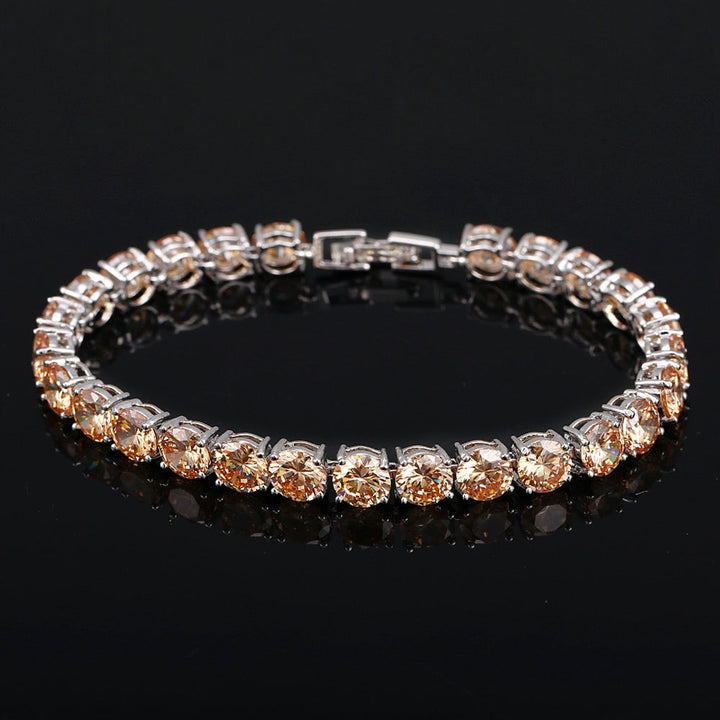 Silbernes Tennisarmband mit runden, champagnerfarbenen Zirkonia-Steinen auf schwarzem Hintergrund.