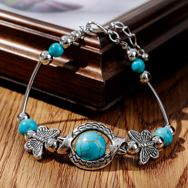 Silberarmband mit türkisfarbenen Steinen und Schmetterlingsanhängern auf Holzhintergrund.