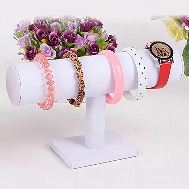 Weißer Samt-Uhrenständer mit Armbändern und Uhr, Schmuckdisplay, dekorative Blumen im Hintergrund.