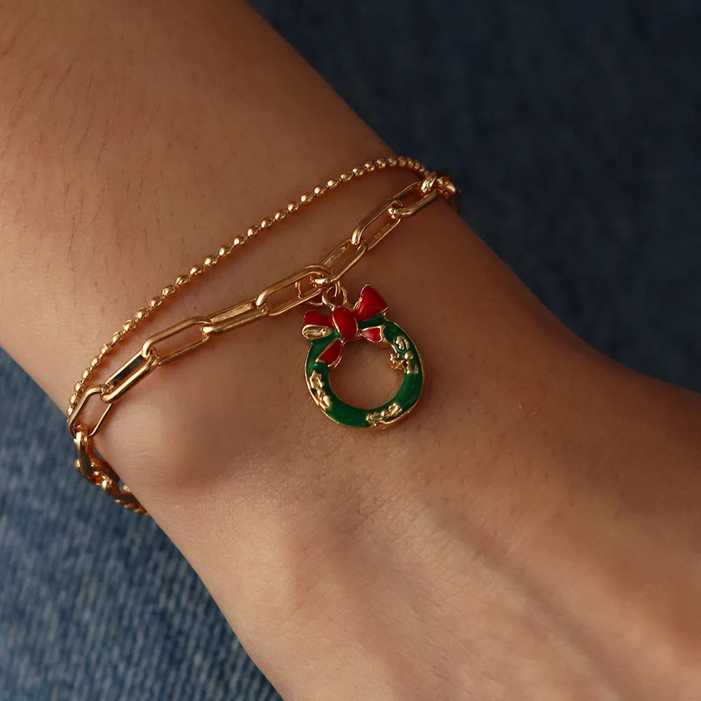 Goldenes Armband mit grünem Weihnachtskranz-Anhänger und roter Schleife auf Handgelenk.