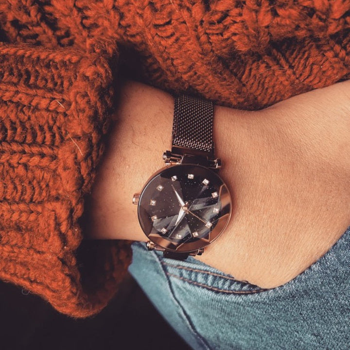 Armbanduhr mit schwarzem Zifferblatt und Metallarmband, getragen auf gestricktem Pullover.