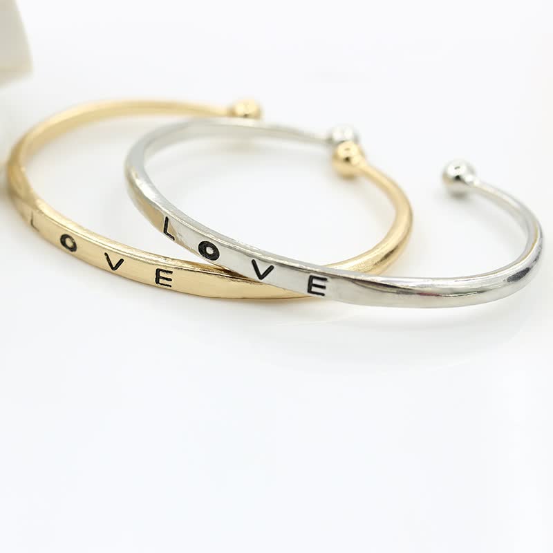 Zwei Armreifen aus Gold und Silber mit "LOVE"-Gravur, modisches Schmuck-Accessoire.