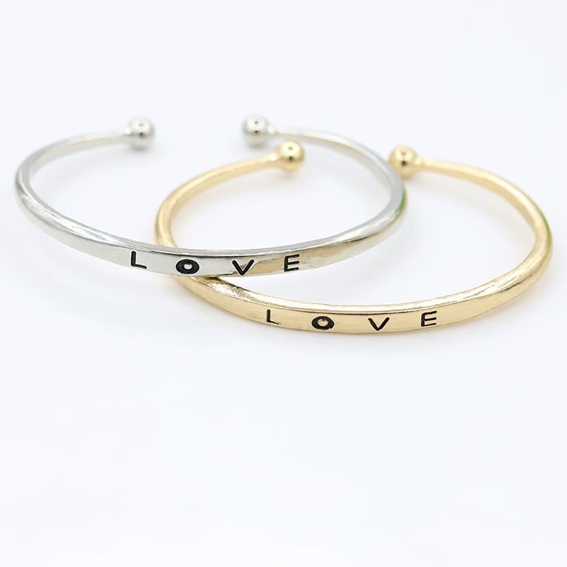 Zwei Armreifen aus Silber und Gold mit "LOVE"-Gravur, modisches Schmuck-Accessoire.