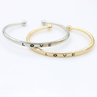 Zwei Armreifen aus Silber und Gold mit "LOVE"-Gravur, modisches Schmuck-Accessoire.