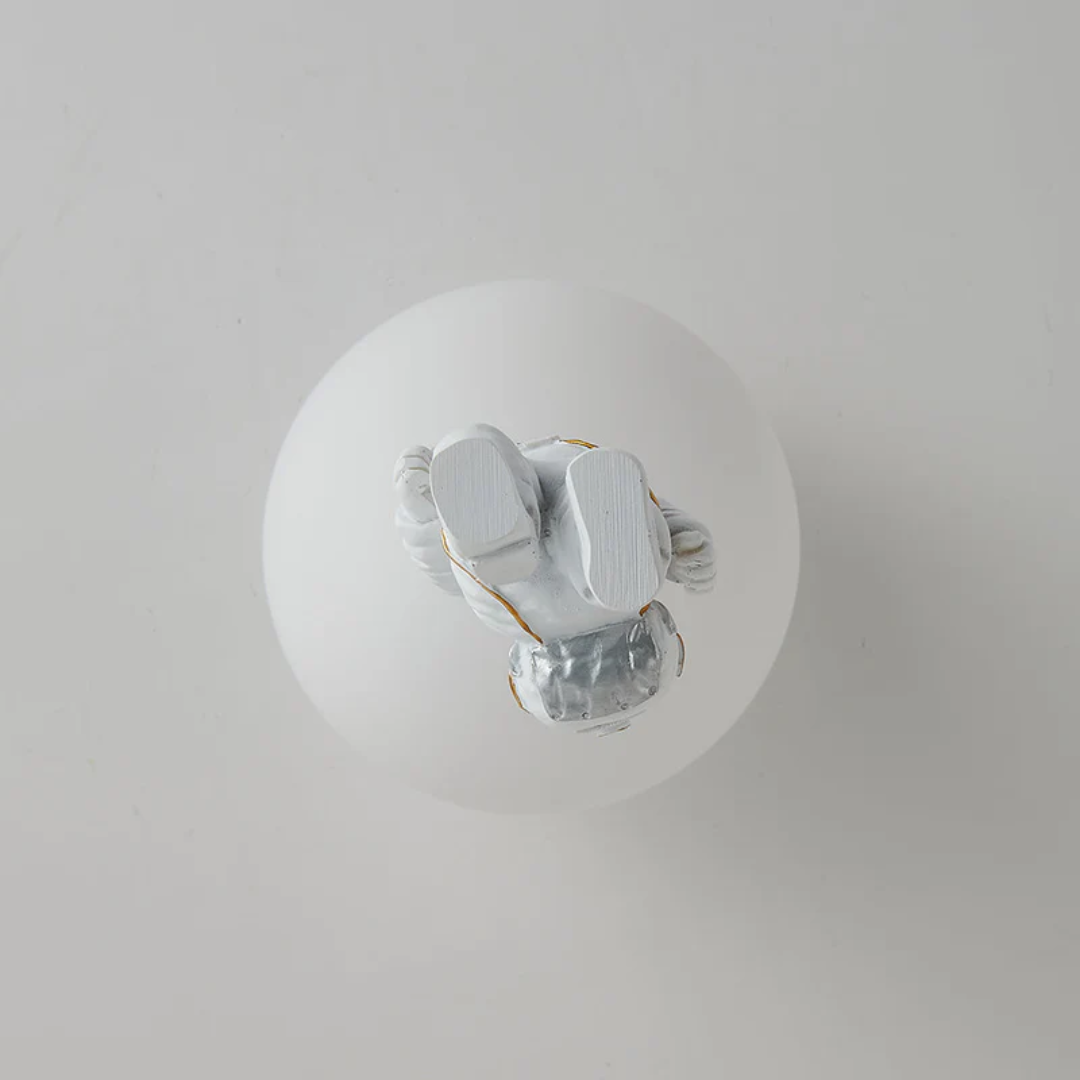 Weiße Glaskugel mit silberner Astronautenfigur, moderne Dekoration, minimalistisches Design.