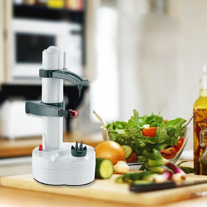 Elektrischer Obst- und Gemüseschäler, weiß, auf Küchentheke neben Salat und Gemüse.