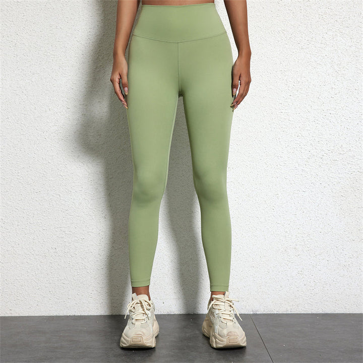 Frau in grüner Leggings und weißen Turnschuhen vor weißer Wand.