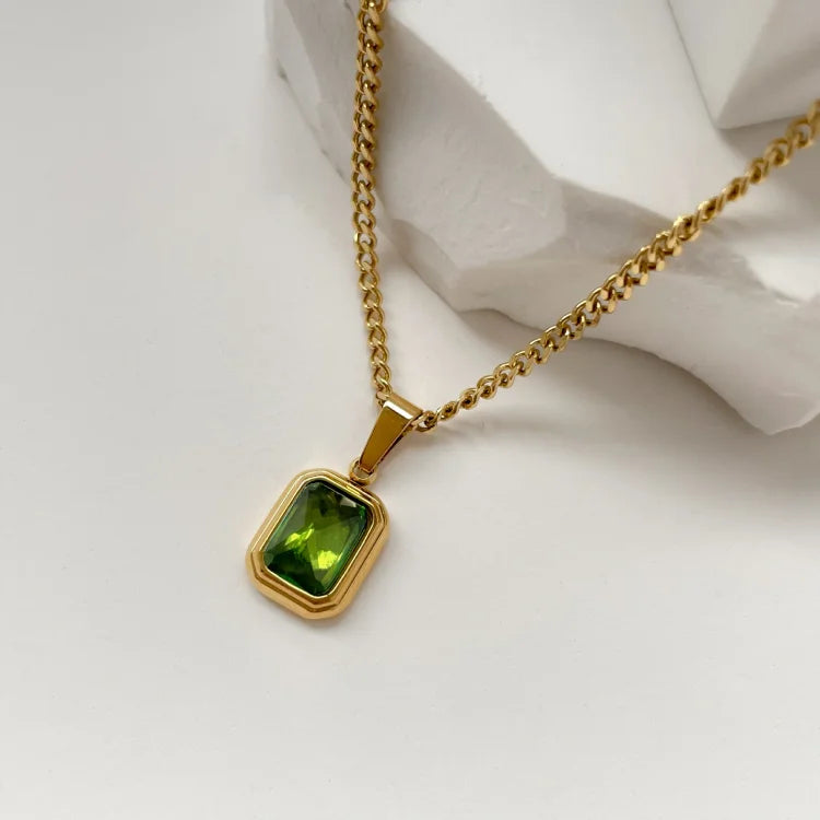 Goldene Halskette mit rechteckigem grünem Edelstein-Anhänger auf weißem Hintergrund.