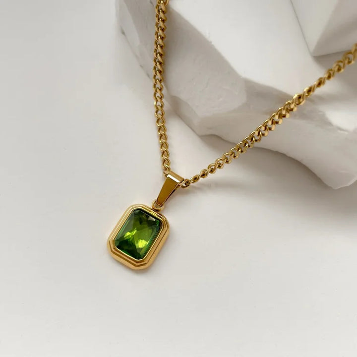 Goldene Halskette mit rechteckigem grünem Edelstein-Anhänger auf weißem Hintergrund.