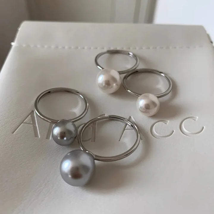 Silberne Ringe mit weißen und grauen Perlen auf weißem Hintergrund, eleganter Schmuck.