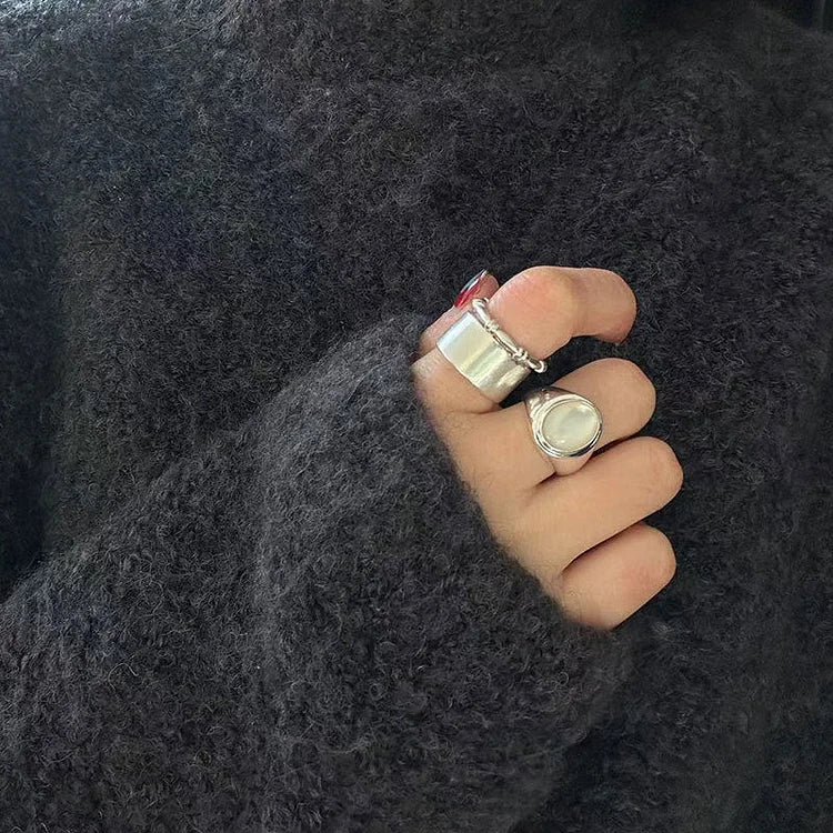 Hand mit silbernen Ringen, getragen auf einem dunklen, flauschigen Pullover.