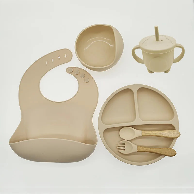 Beiges Silikon-Babygeschirr-Set mit Lätzchen, Teller, Schüssel, Becher und Besteck.