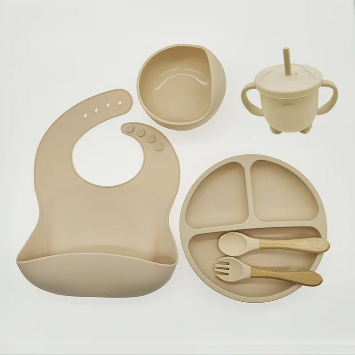 Beiges Silikon-Babygeschirr-Set mit Lätzchen, Teller, Schüssel, Becher und Besteck.