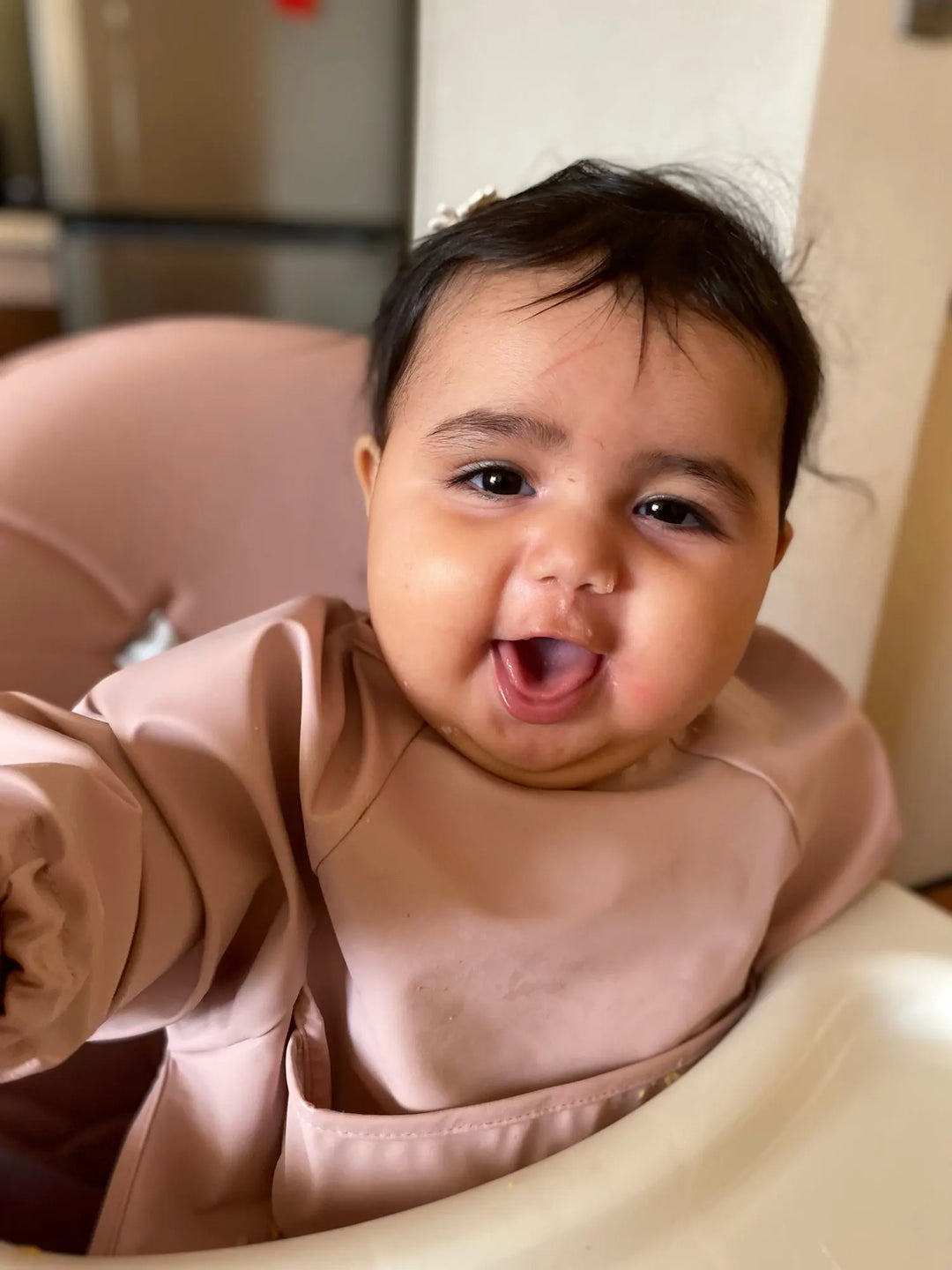 Kleinkind in rosa Lätzchen, lächelnd im Hochstuhl, Baby-Mode, niedlich, Innenraum.