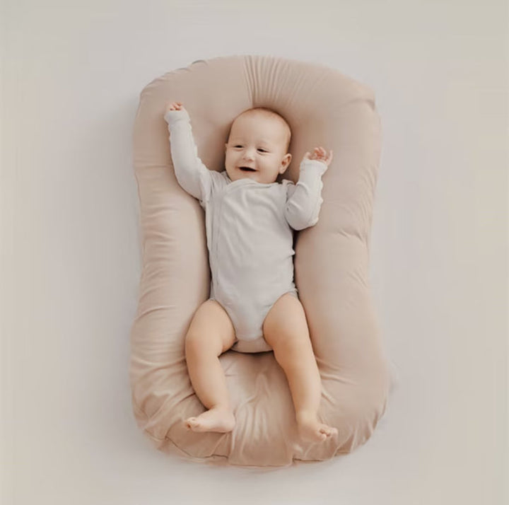 Lächelndes Baby in beigem Babynest, weicher Stoff, gemütlich, sicherer Schlafplatz.