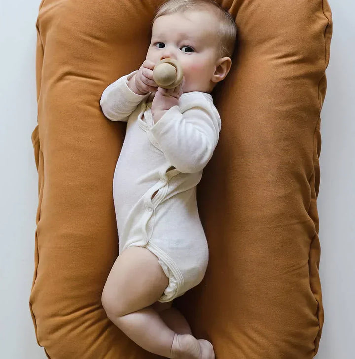 Baby in weißem Strampler auf braunem Babynest, trinkt aus Flasche, gemütlich, Neugeborenenpflege.