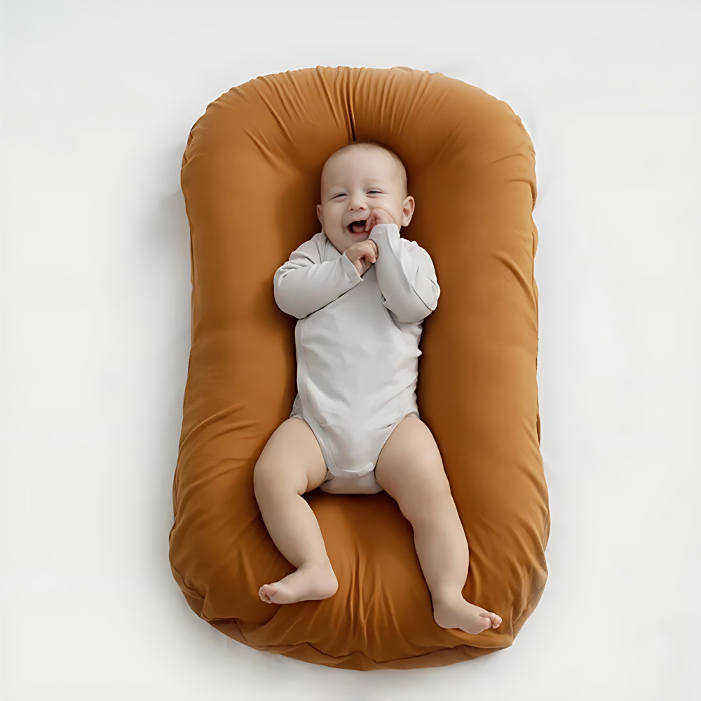 Lachendes Baby in weißem Strampler auf braunem Babynest, gemütlich, weich, sicher.