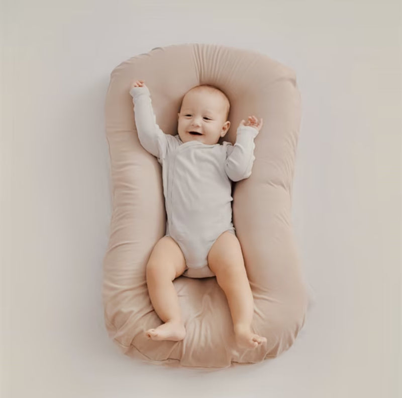 Lächelndes Baby in beigem Babynest, weich, bequem, ideal für Neugeborene, Schlafunterstützung.