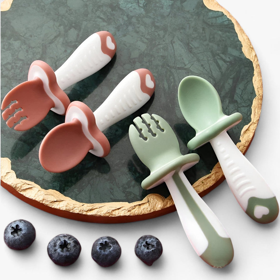 Baby Besteck Set aus Silikon in Rosa und Grün auf Marmorplatte, ergonomisch, BPA-frei.