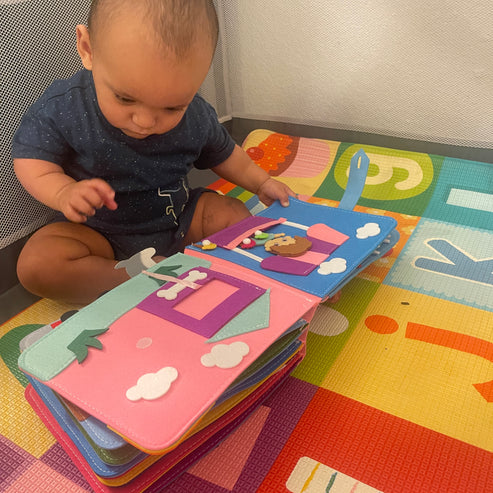 Kleinkind spielt mit buntem Filz-Bilderbuch auf Spielmatte im Kinderzimmer.