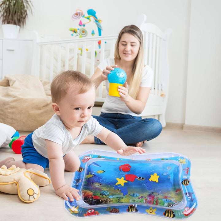 Kleinkind spielt mit Wasser-Spielmatte im Kinderzimmer, Mutter im Hintergrund, bunte Fische.