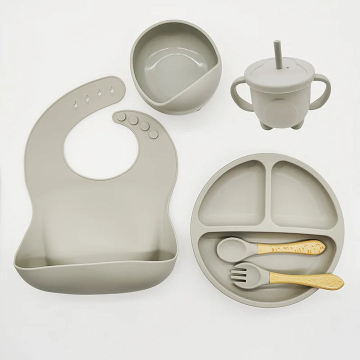 Graues Silikon-Babygeschirr-Set mit Lätzchen, Teller, Schüssel, Becher und Besteck.