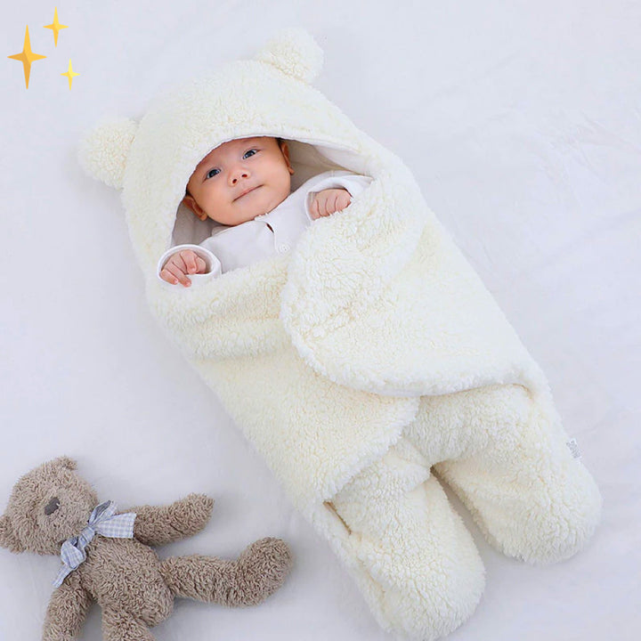 Baby in weißem Plüsch-Babysack mit Kapuze und Bärenohren, auf weißem Hintergrund.