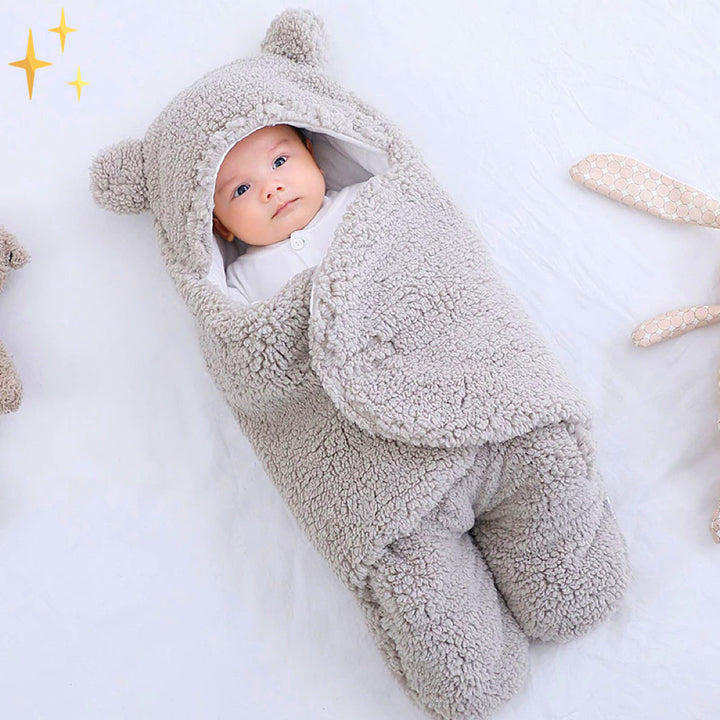 Baby in grauem, flauschigem Babyschlafsack mit Kapuze und Bärenohren, gemütlich und warm.