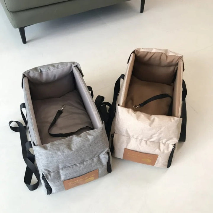 Zwei tragbare Babytragetaschen, grau und beige, mit Sicherheitsgurten auf weißem Boden.