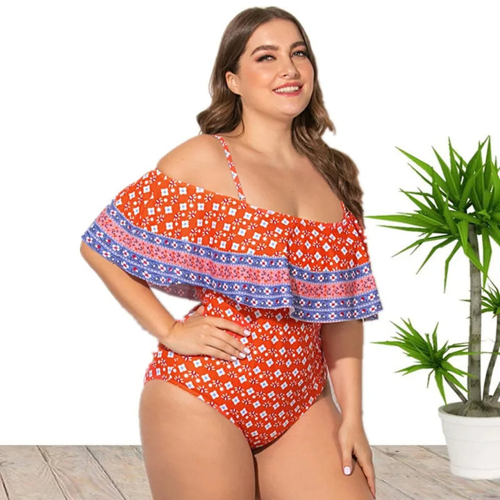 Frau im roten Badeanzug mit blauem Muster, Off-Shoulder-Design, lächelnd, vor weißem Hintergrund.