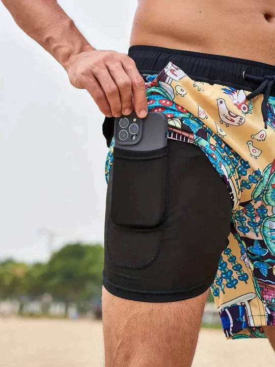 Mann in bunten Badeshorts mit Smartphone-Tasche am Strand.