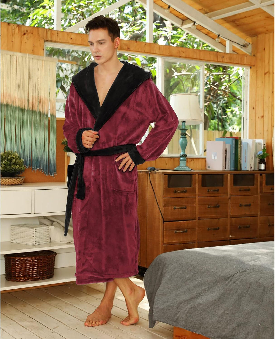 Mann im weinroten Fleece-Bademantel mit schwarzem Kragen, stehend im Schlafzimmer.
