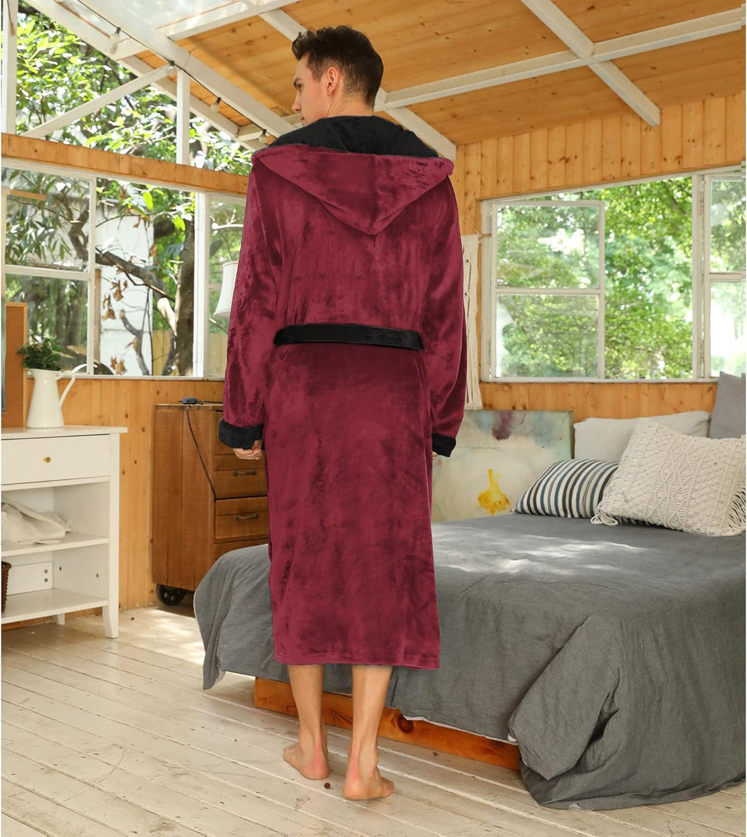 Mann im roten Fleece-Bademantel mit Kapuze im Schlafzimmer, gemütliche Morgenroutine.