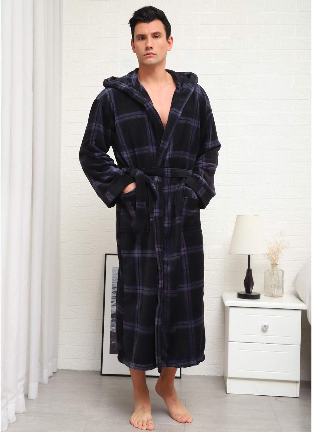 Mann im karierten Bademantel mit Kapuze, schwarz-blau, aus Fleece, stehend im Schlafzimmer.