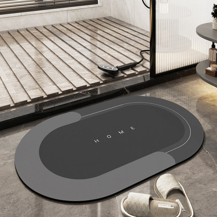 Grauer rutschfester Badezimmerteppich oval mit "Home"-Aufdruck auf Marmorfliesen.