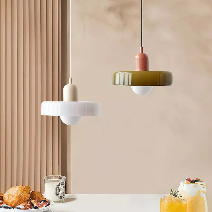 Zwei Bauhaus-Pendelleuchten, weiß und olivgrün, über einem Tisch mit Frühstück.