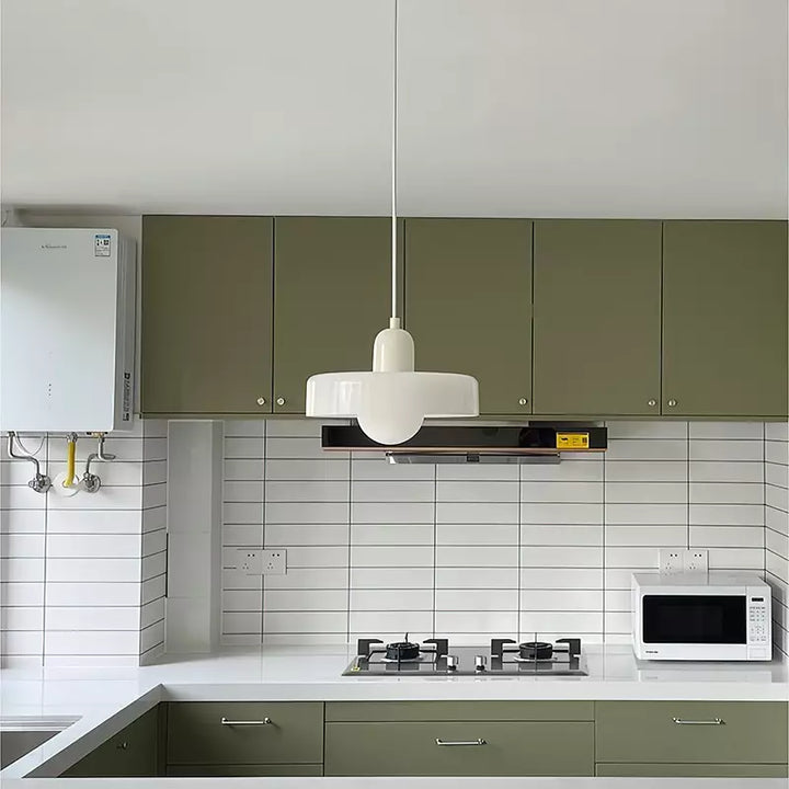 Weiße Pendelleuchte im Bauhaus-Stil über moderner Küche mit grünen Schränken und Mikrowelle.