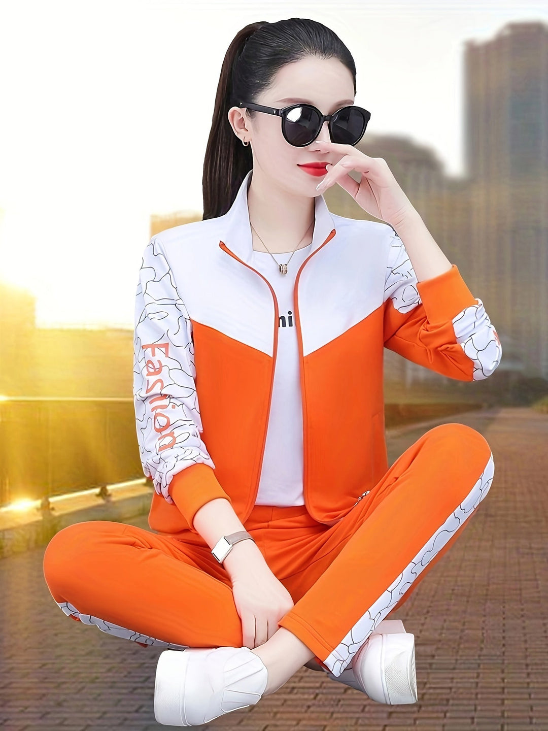 Frau in orange-weißem Trainingsanzug mit Sonnenbrille, sitzt im Freien, modisch, sportlich.