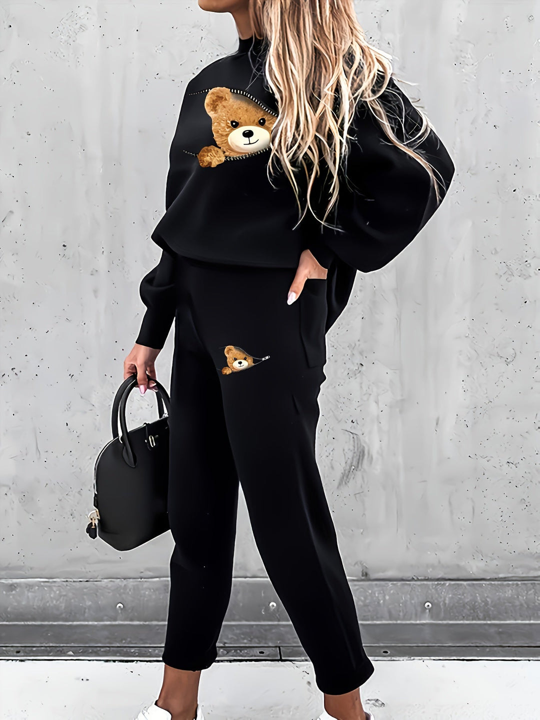 Frau in schwarzem Teddy-Print-Sweatshirt und Hose, hält schwarze Handtasche.