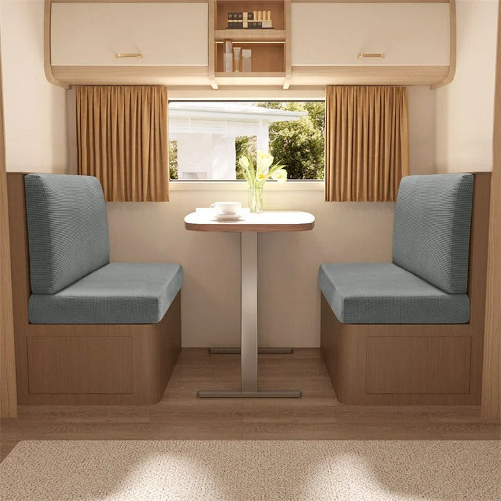 Wohnmobil-Sitzgruppe mit grauen Polstern, Holztisch, Vorhängen, ideal für Campingreisen.