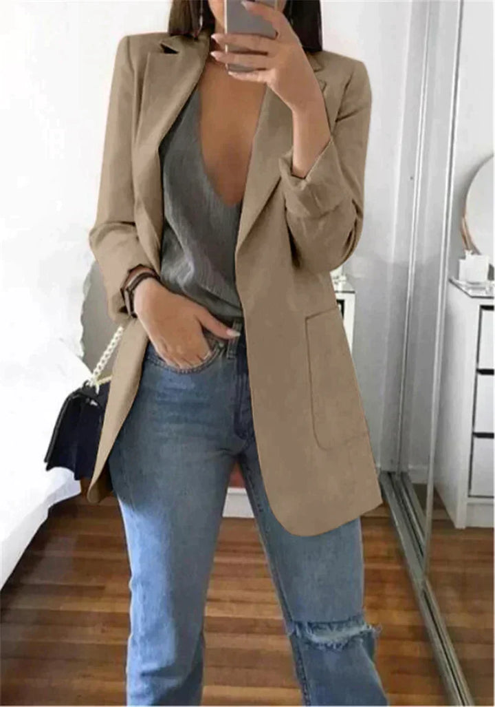 Frau in beigem Blazer, grauem Top und blauer Jeans, modisches Outfit, Spiegel-Selfie.