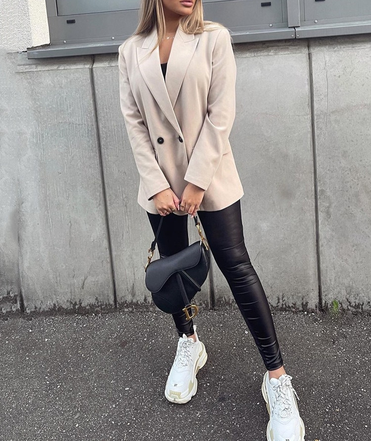 Frau in beigem Blazer, schwarze Lederleggings, weiße Sneaker, schwarze Umhängetasche.
