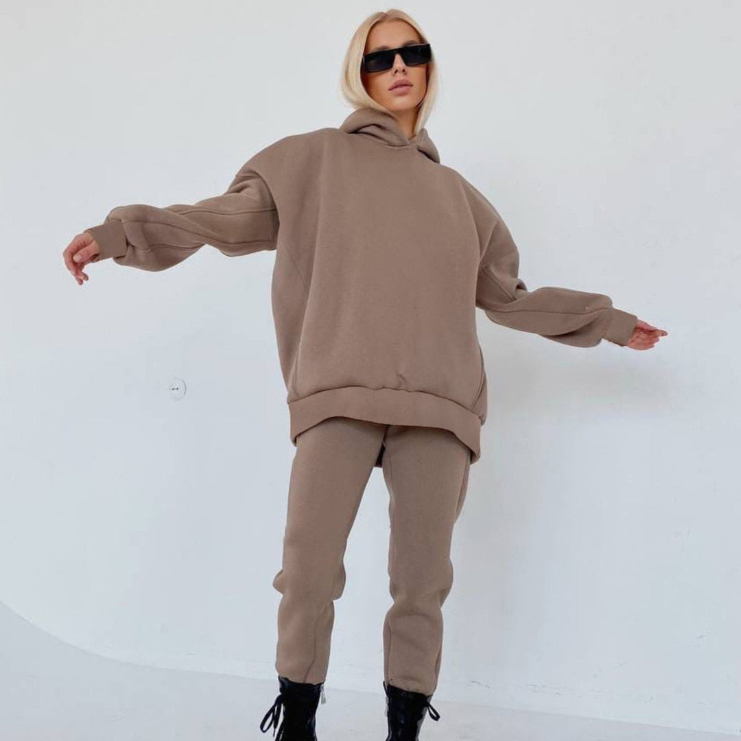 Frau in beigem Oversize-Sweatshirt und Jogginghose, schwarze Stiefel, Sonnenbrille.