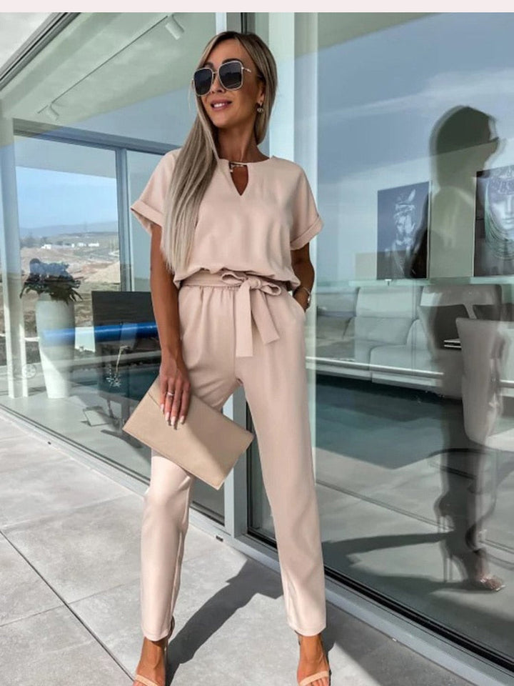 Frau in beigem Jumpsuit mit Sonnenbrille und Clutch, moderne Mode, Sommeroutfit, Terrasse.