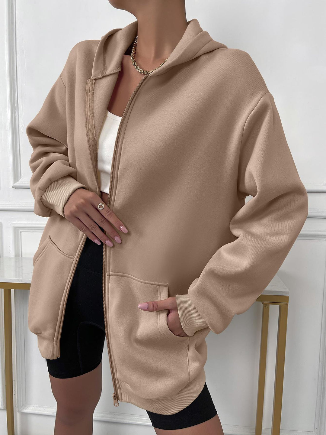 Frau trägt beige Kapuzenjacke, Reißverschluss, lässig, modisch, Damenmode, Streetwear.