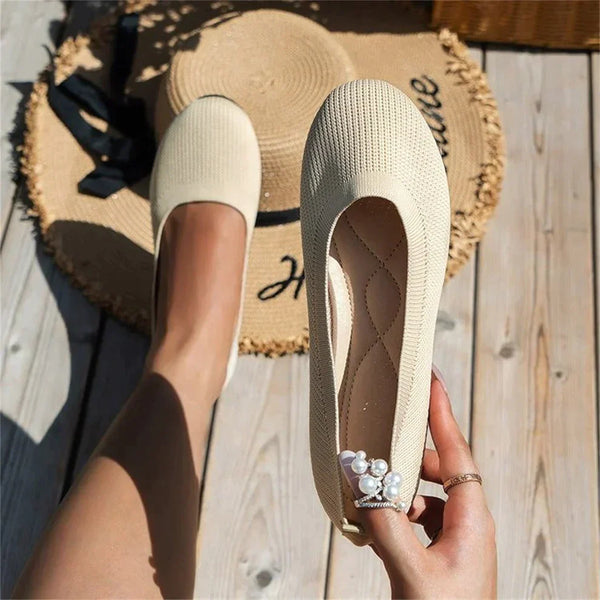 Beige Damen-Ballerinas aus Strickstoff, flach, mit Perlenring, auf Holzterrasse.